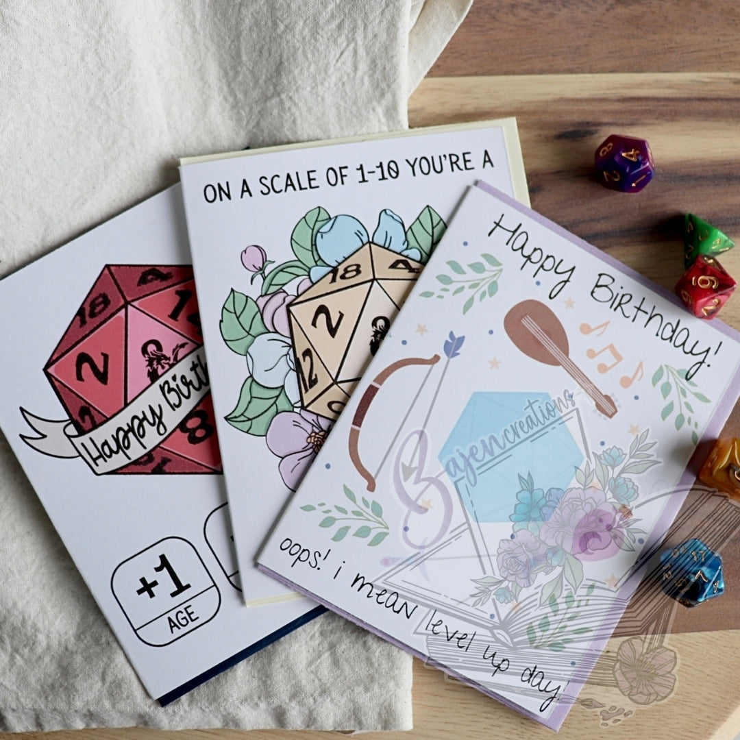 Three birthday cards with playful dungeons and dragons designs on a wooden surface.