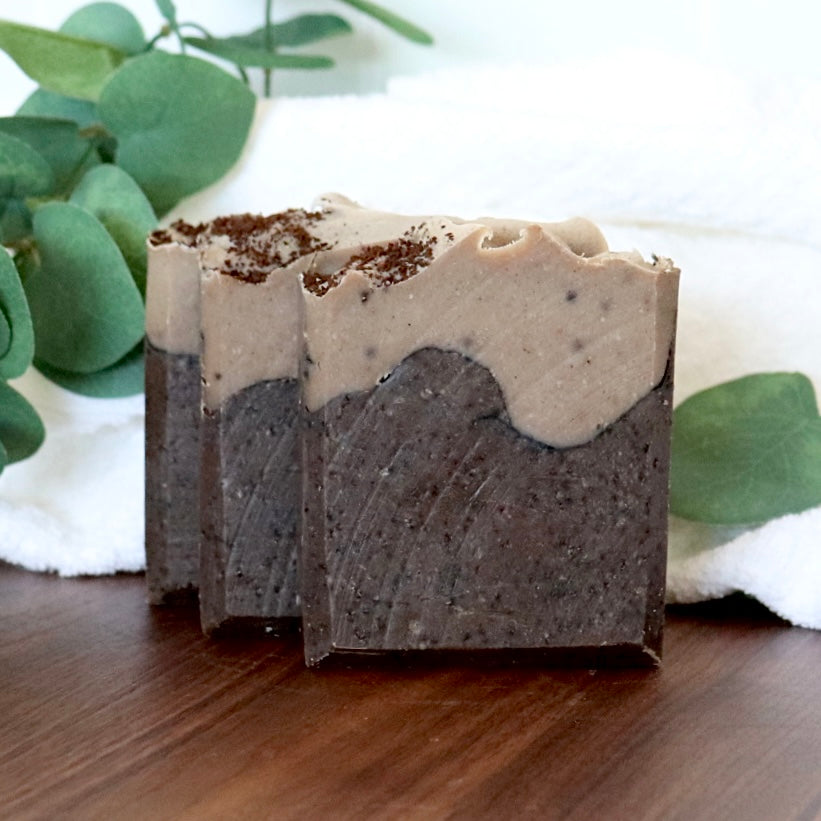 Two layered soap bars on a wooden surface with green leaves in the background