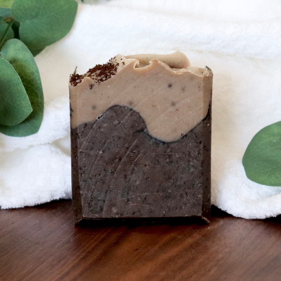 Two-layered soap bar with green leaves and white fabric in the background