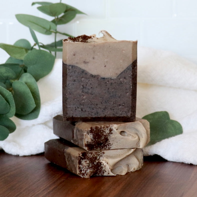 Stack of layered soap bars on a wooden surface with greenery in the background