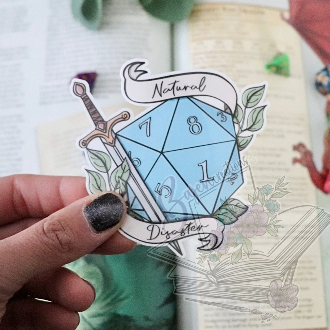 Sticker of a blue die with sword and banner held by a hand over a notebook.