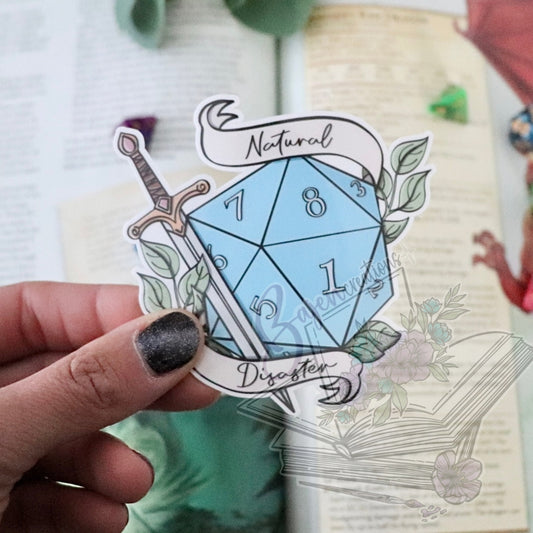 Sticker of a blue die with sword and banner held by a hand over a notebook.
