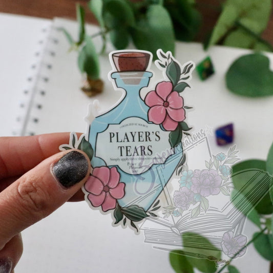Sticker of a bottle labeled 'Player's Tears' held by a hand with a blurred background